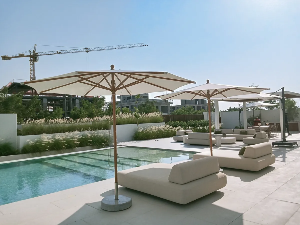 Piazza centre-pole umbrellas over poolside daybeds with lounge seating in the background